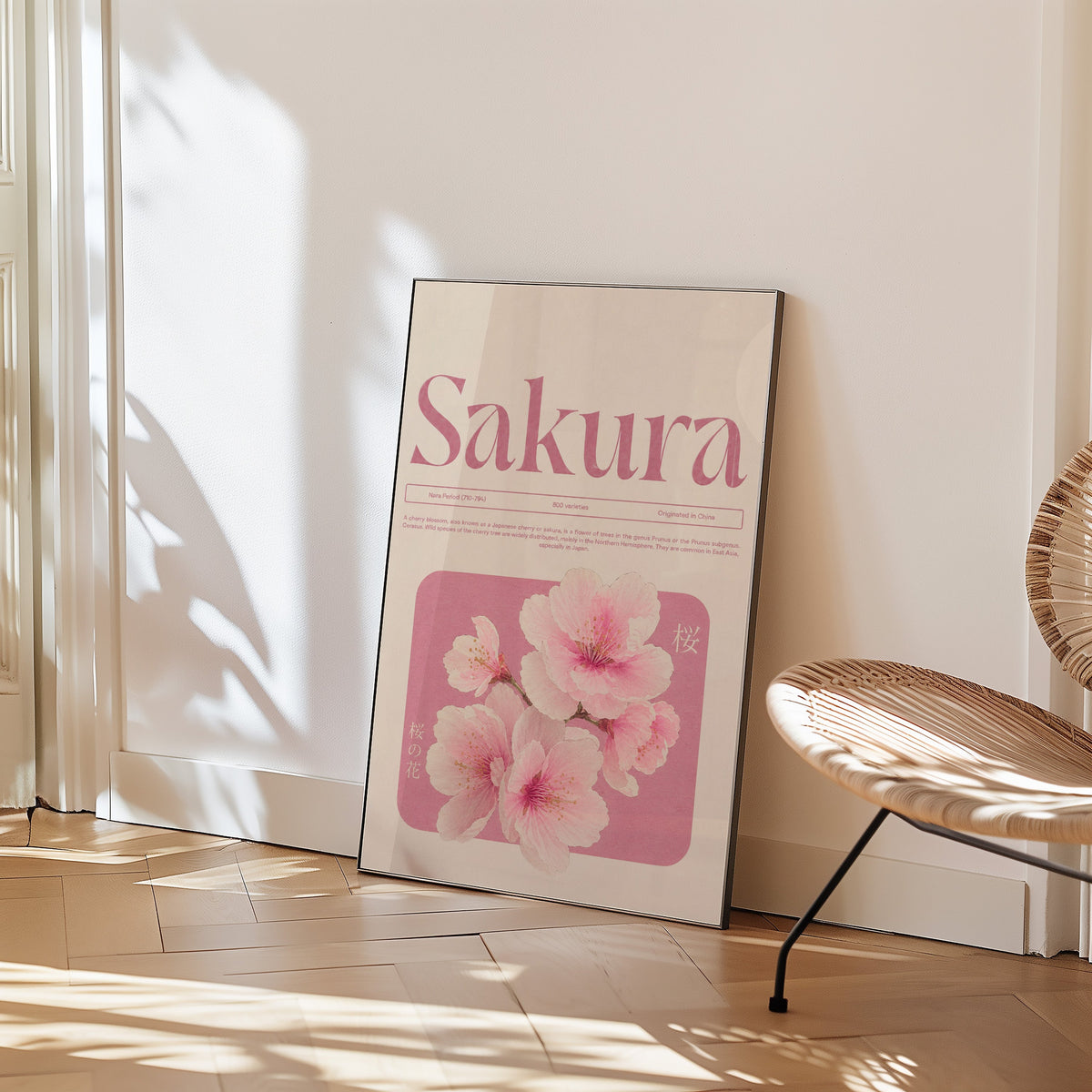 pink sakura blossom typography print in a black frame leaning on a herringbone floor beside a woven rattan chair