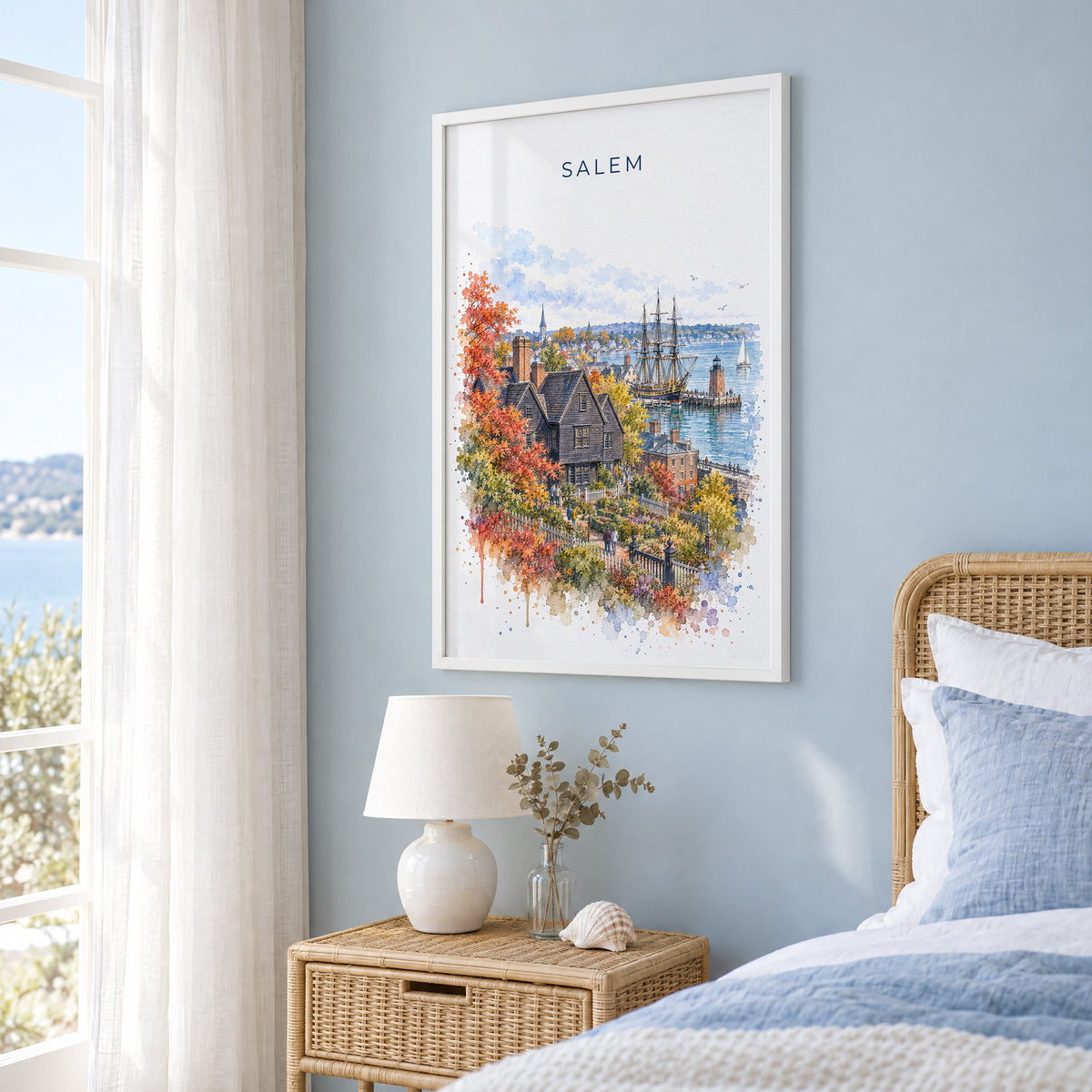 Salem, Massachusetts watercolor print in a white frame on a pale blue wall beside a rattan bed in a coastal bedroom