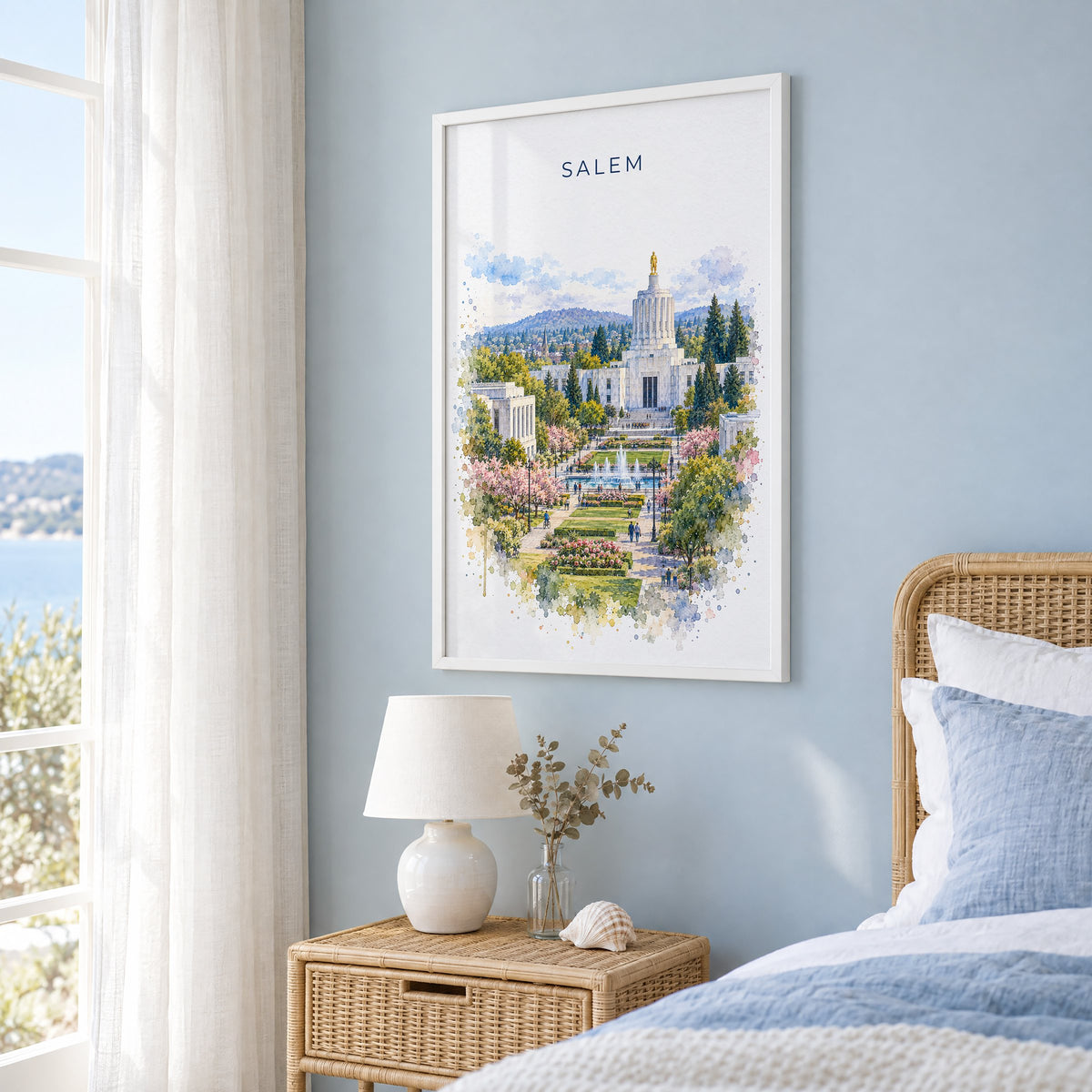 Salem, Oregon watercolor print in a white frame on a pale blue wall beside a rattan bed in a coastal bedroom