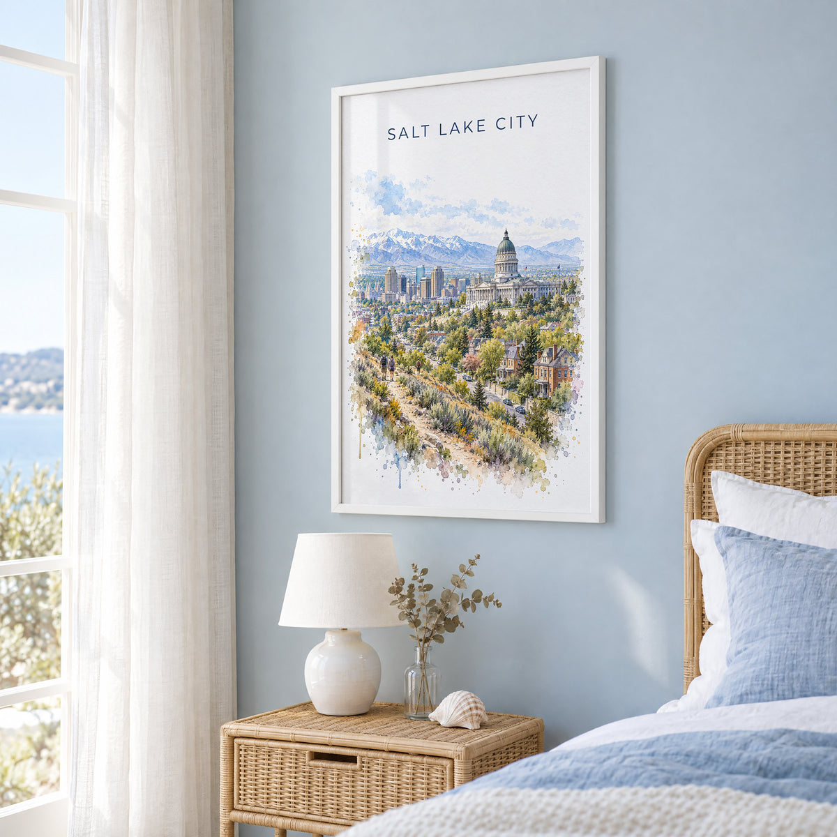 Salt Lake City watercolor print in a white frame on a pale blue wall beside a rattan bed in a coastal bedroom