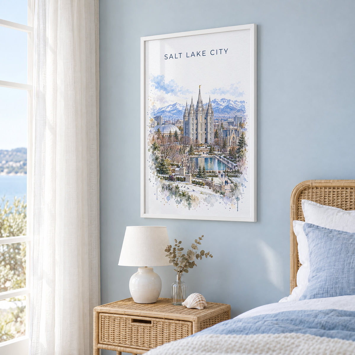 Salt Lake Temple watercolor print in a white frame on a pale blue wall beside a rattan bed in a coastal bedroom