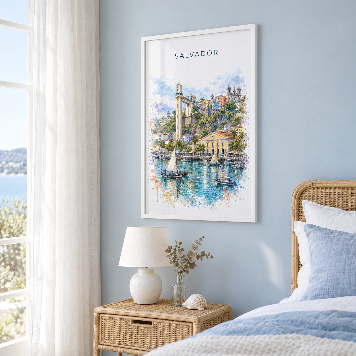 Salvador, Brazil watercolor print in a white frame on a pale blue wall beside a rattan bed in a coastal bedroom