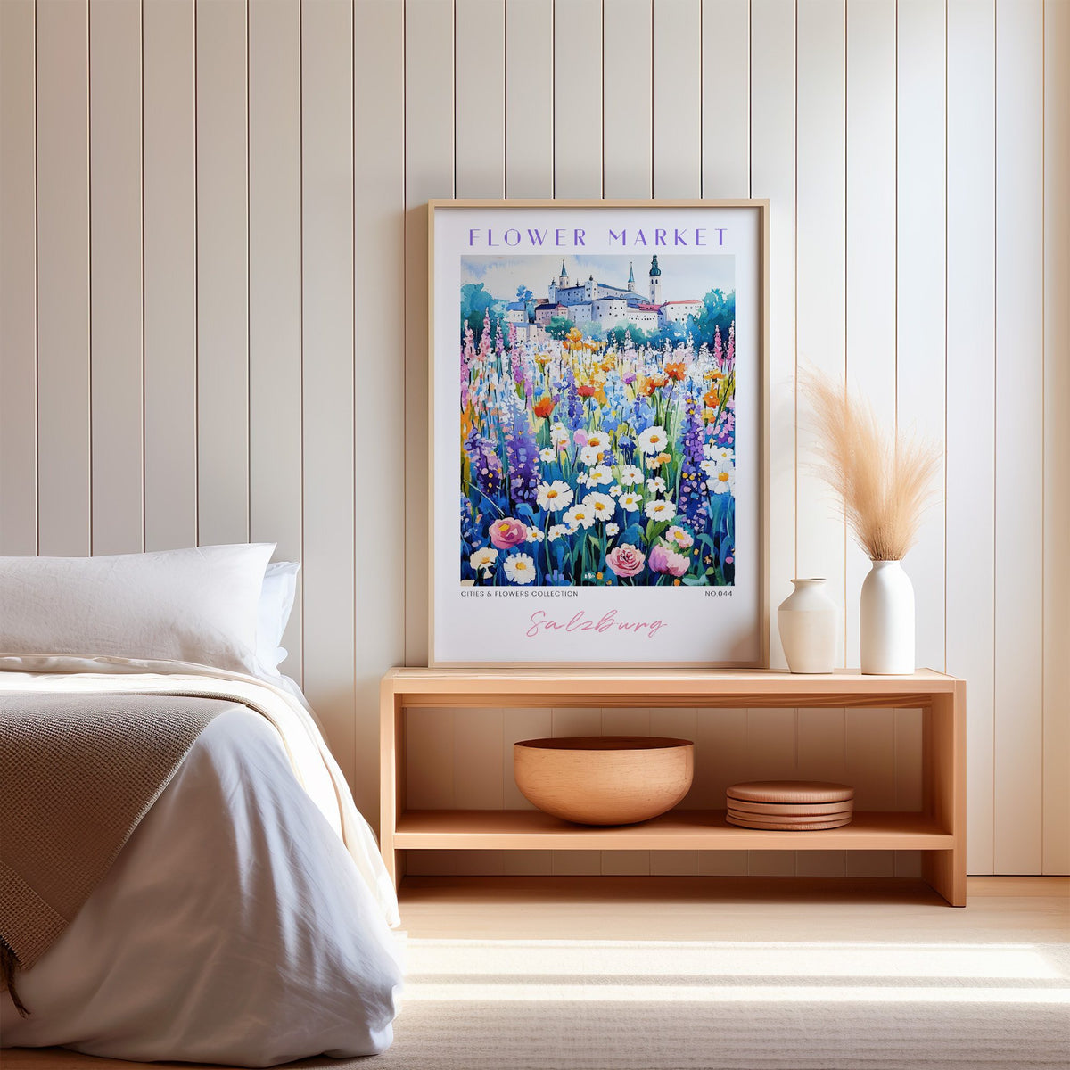 Salzburg flower market print in an oak frame on a wood bench against a white shiplap bedroom wall with pampas grass