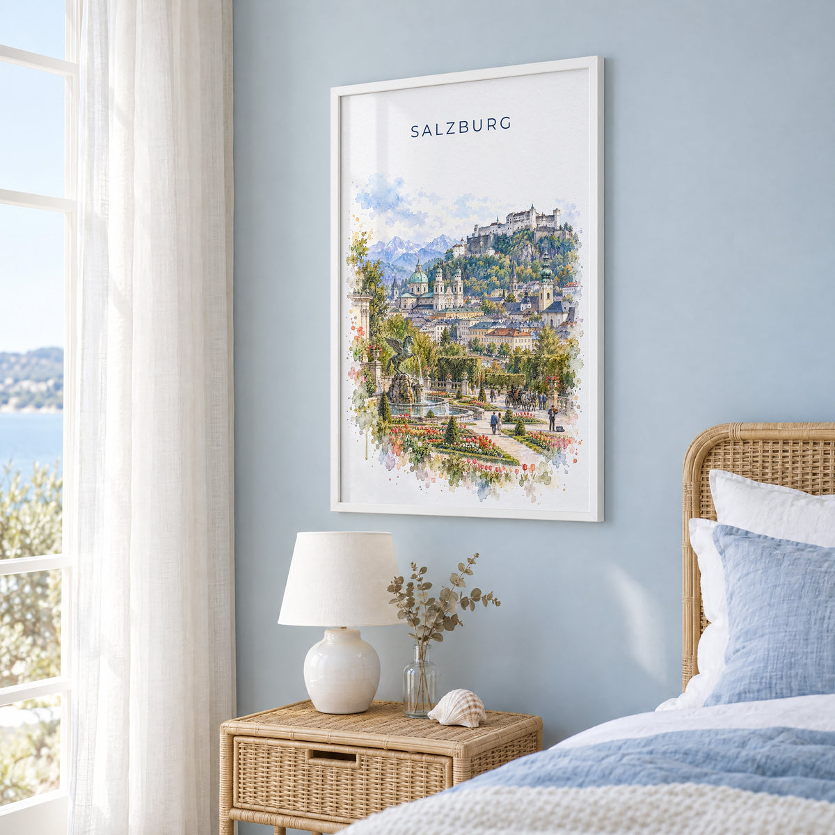 Salzburg watercolor print in a white frame on a pale blue wall beside a rattan bed in a coastal bedroom