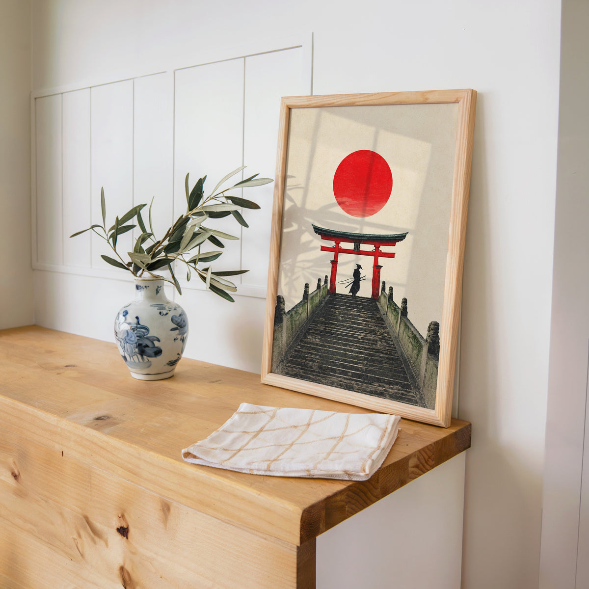 samurai under red torii gate print in a pine frame on a wooden counter beside a blue and white porcelain vase