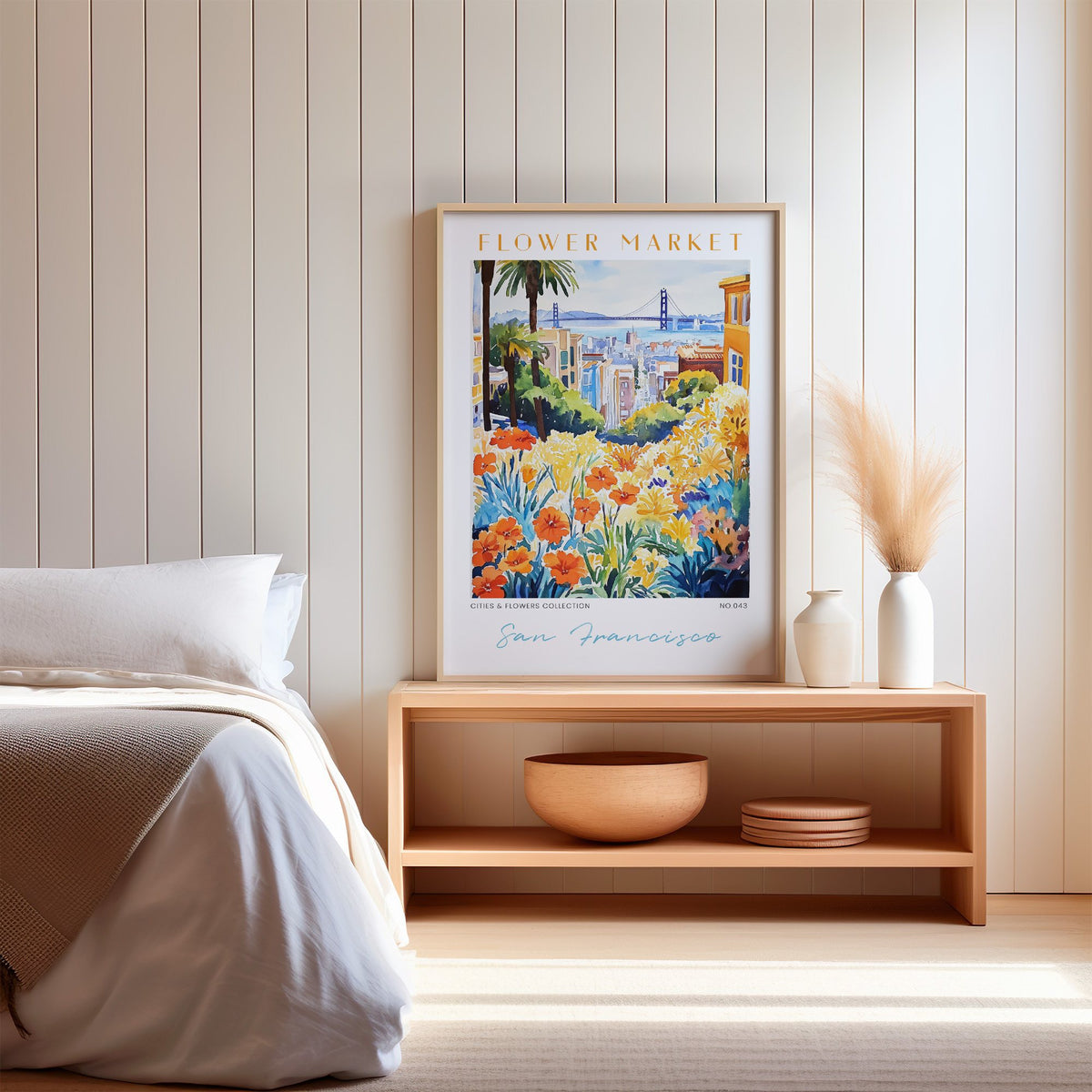 San Francisco flower market print in an oak frame on a wood bench against a white shiplap bedroom wall with pampas grass