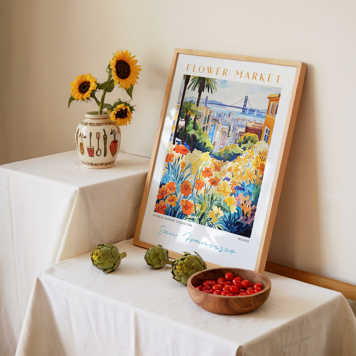 San Francisco flower market print in an oak frame leaning on a linen-draped table beside a vase of sunflowers
