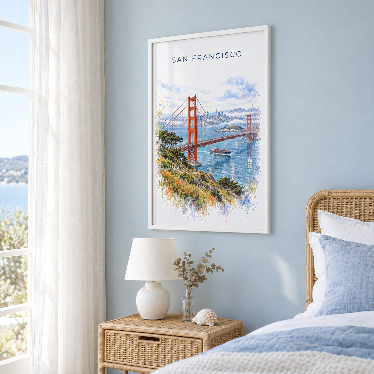 San Francisco watercolor print in a white frame on a pale blue wall beside a rattan bed in a coastal bedroom