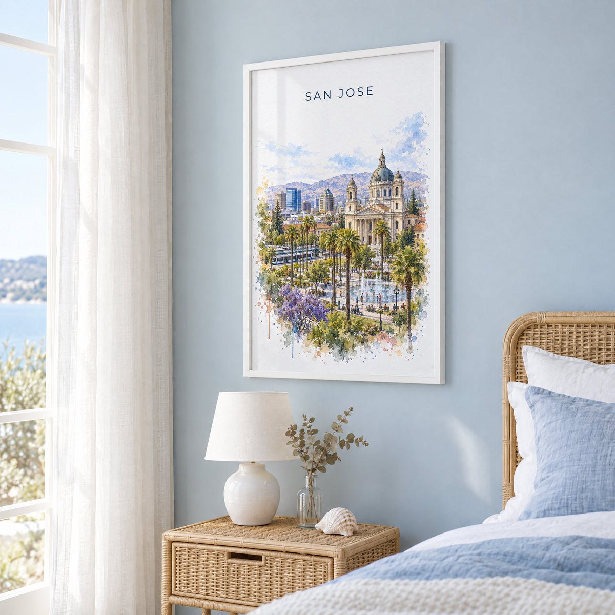 San Jose, California watercolor print in a white frame on a pale blue wall beside a rattan bed in a coastal bedroom