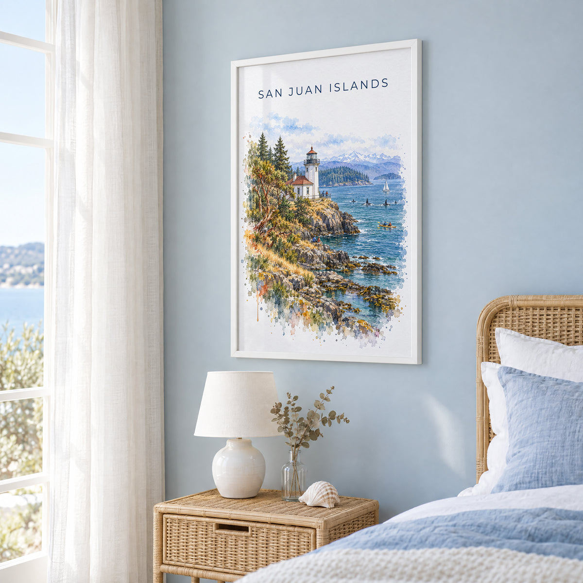 San Juan Islands watercolor print in a white frame on a pale blue wall beside a rattan bed in a coastal bedroom