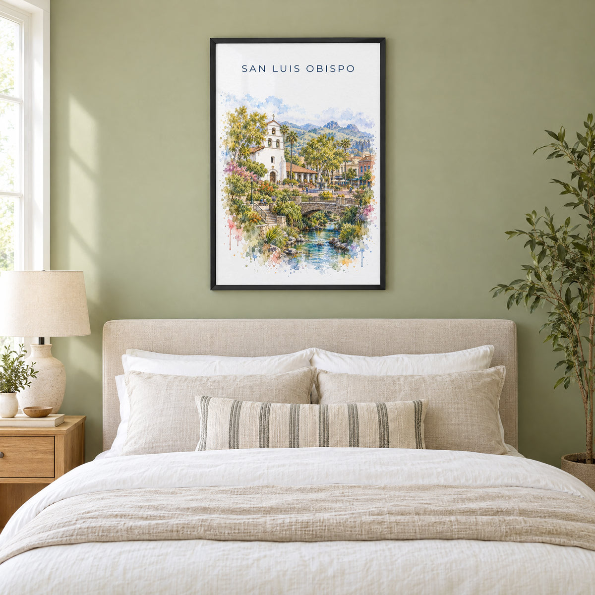 San Luis Obispo watercolor print in a black frame above an upholstered headboard in a sage green bedroom