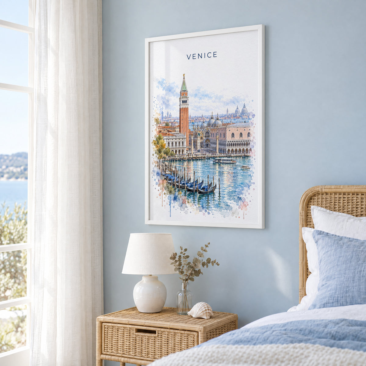St. Mark's Square Venice watercolor print in a white frame on a pale blue wall beside a rattan bed in a coastal bedroom