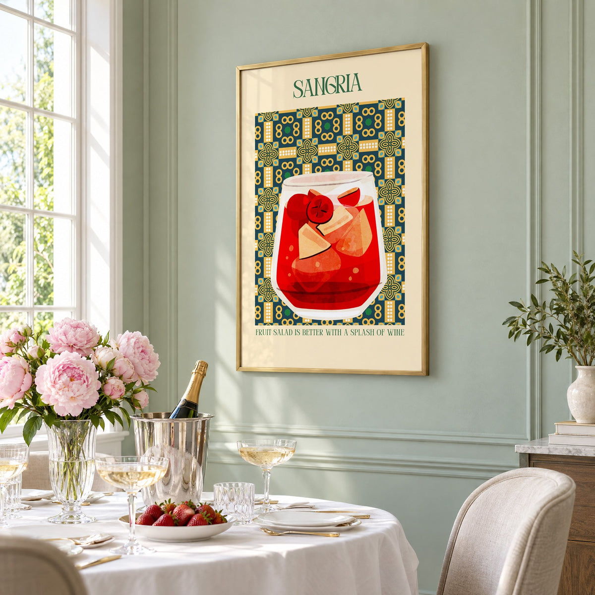 SANGRIA red glass patterned tile print in a brass frame on a sage wall above a brunch table with champagne and peonies, seen at an angle