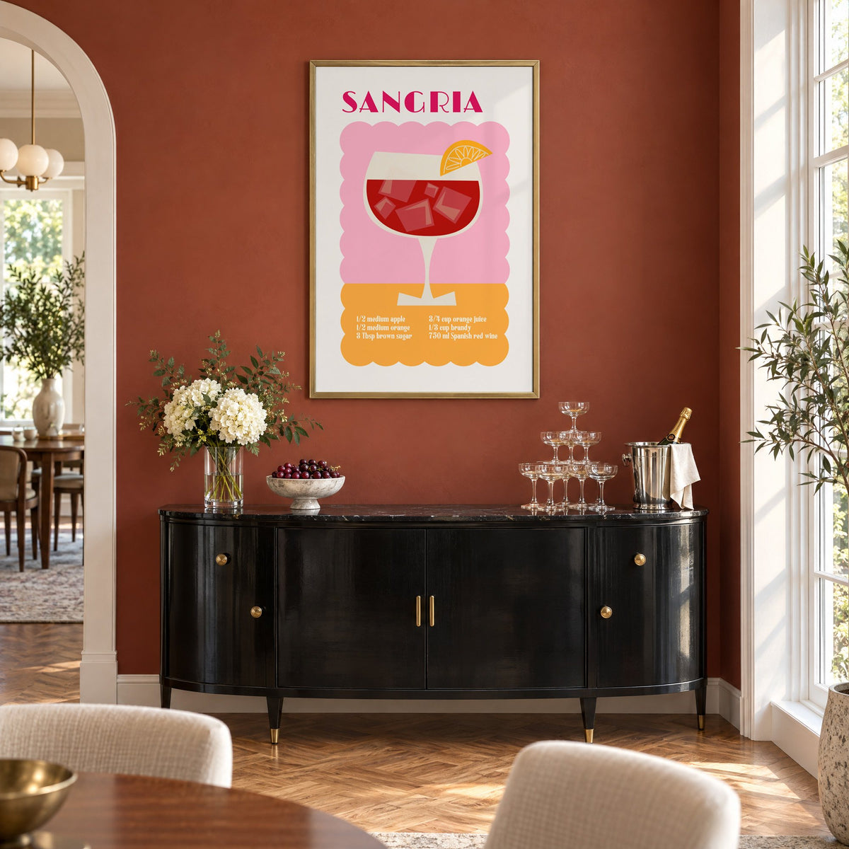 SANGRIA recipe pink and orange print in a brass frame on a terracotta wall above a black buffet with a champagne tower