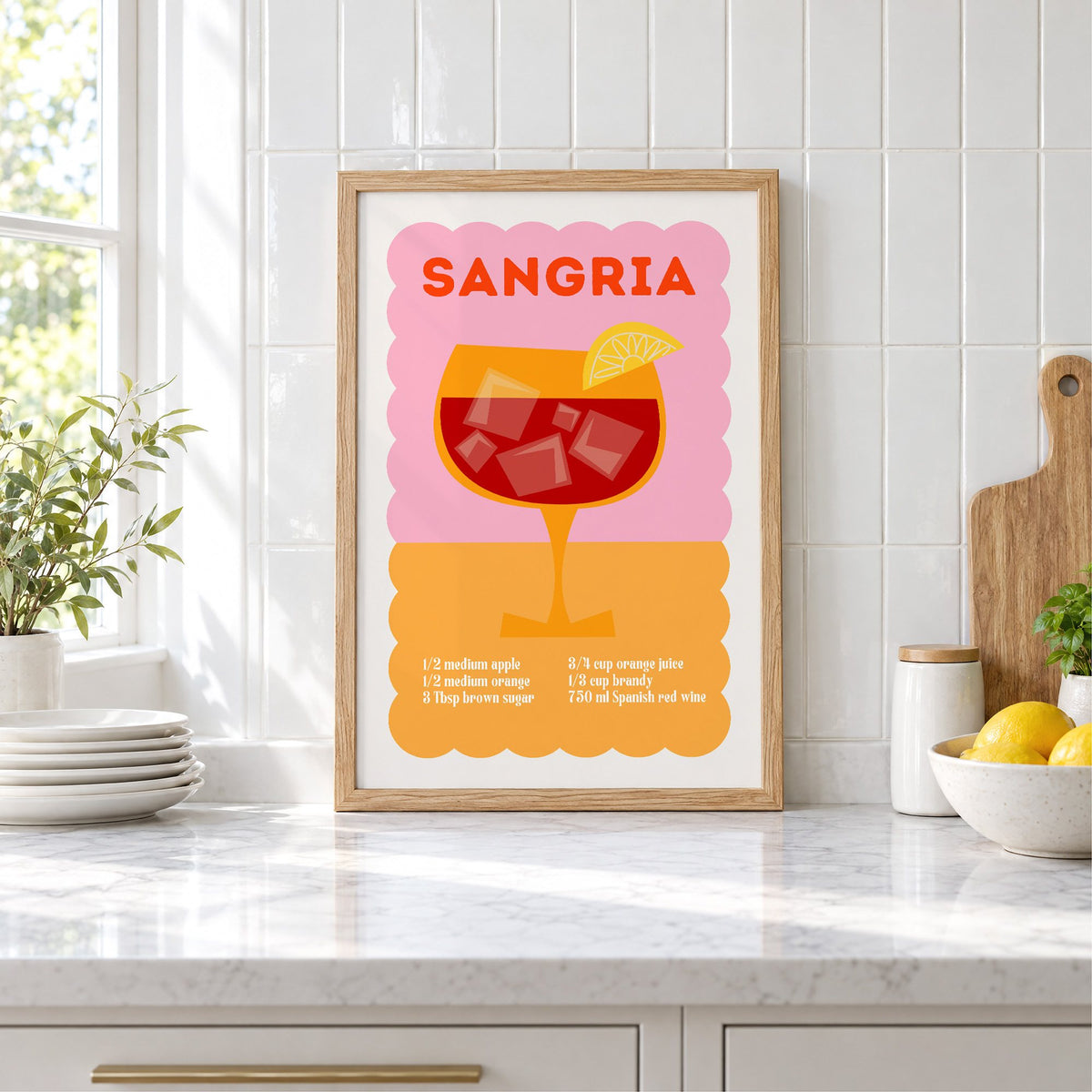 Sangria recipe pink and orange print in an oak frame leaning on a marble counter by white tiles and lemons