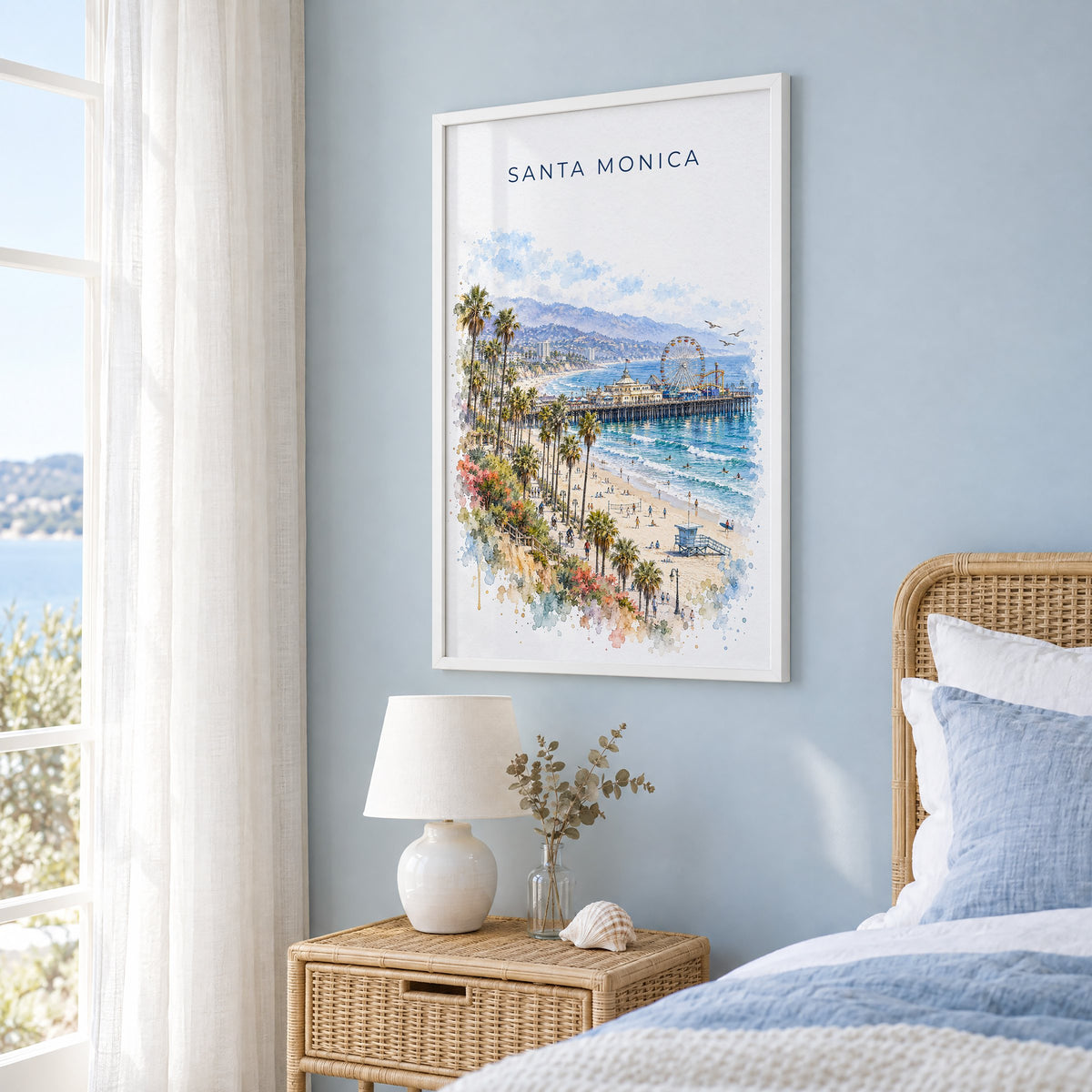 Santa Monica watercolor print in a white frame on a pale blue wall beside a rattan bed in a coastal bedroom