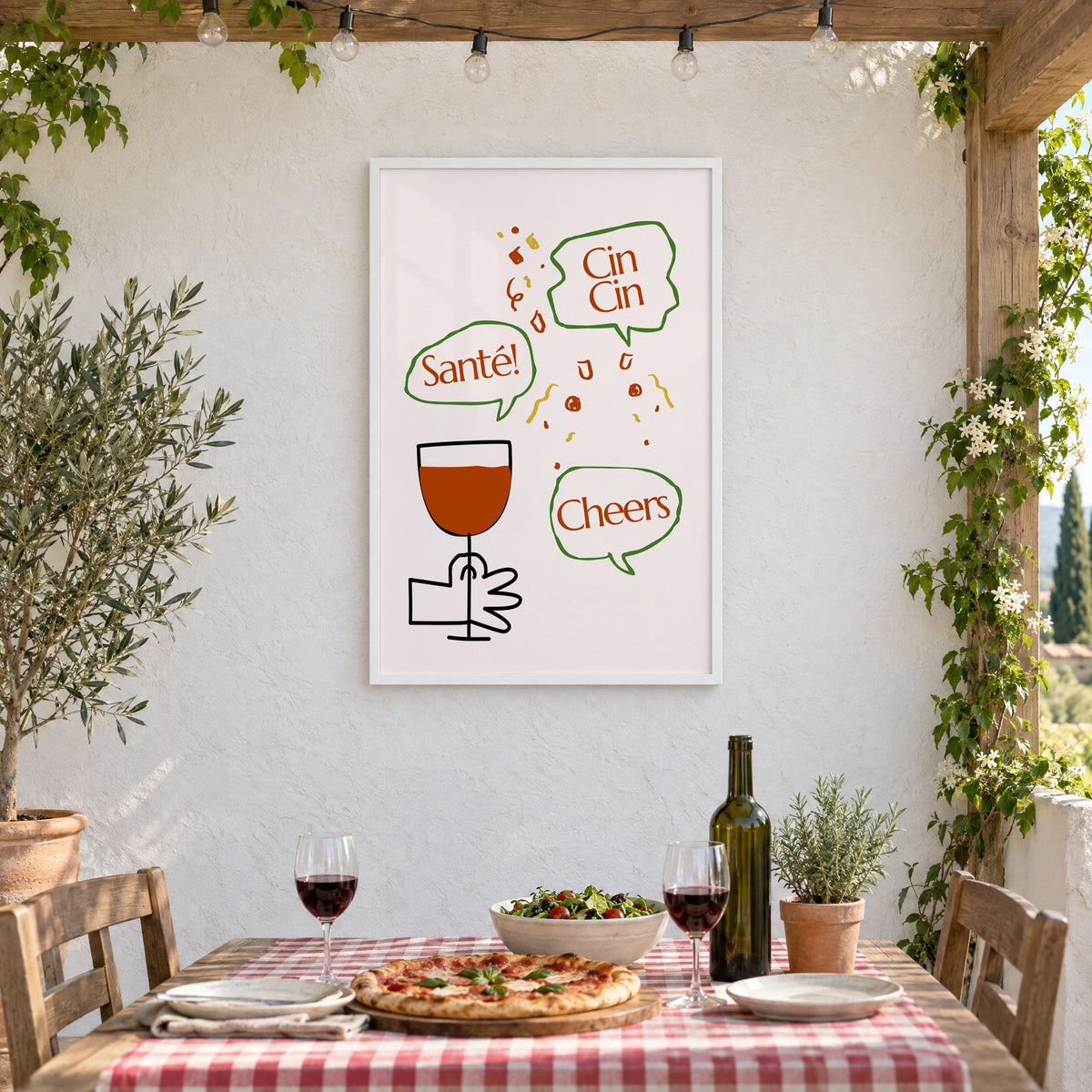 Cin Cin Santé Cheers speech bubbles wine print in a white frame on a stucco wall above a checked-cloth table with pizza and red wine