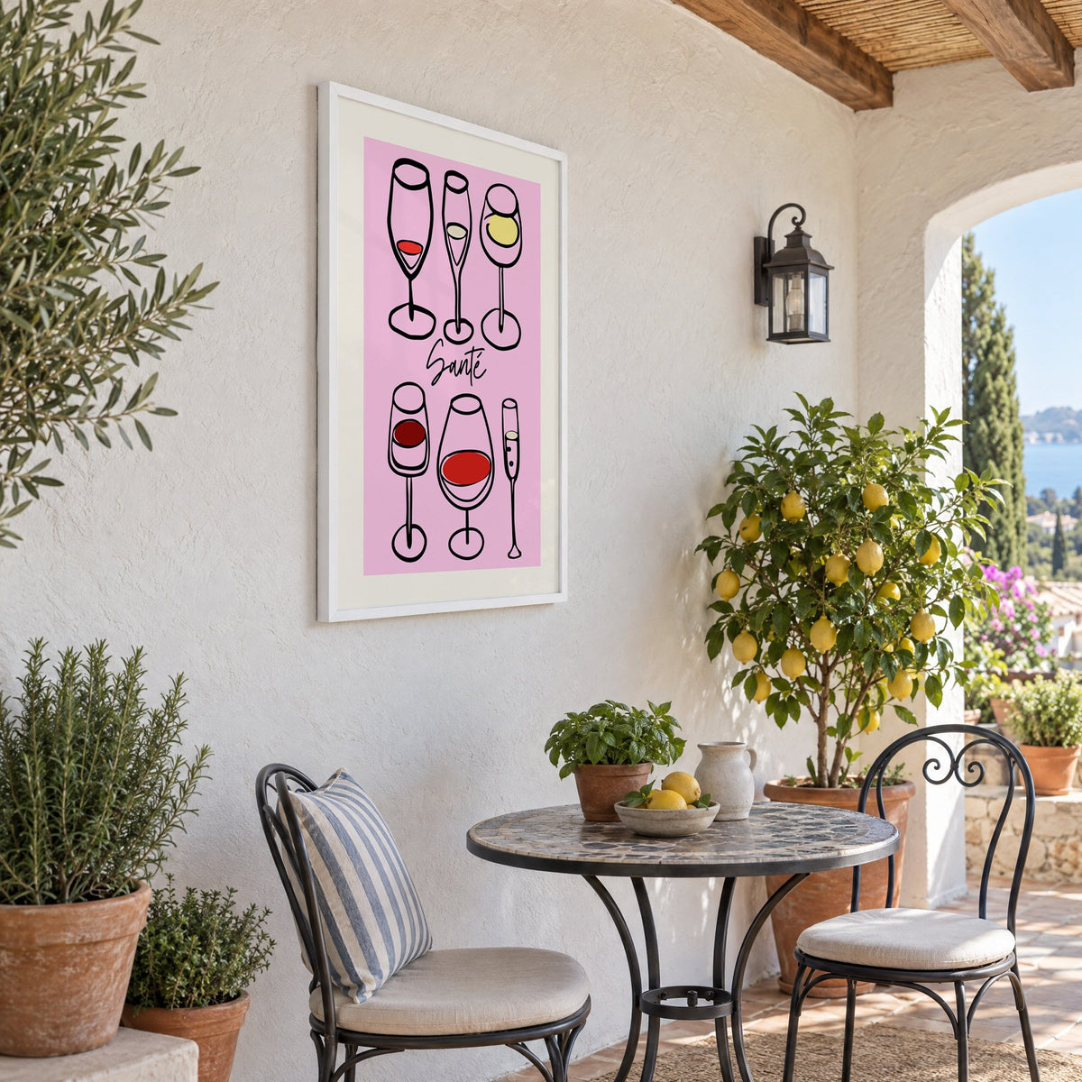 Santé wine glasses line art print in a white frame on a sunny patio wall beside a potted lemon tree