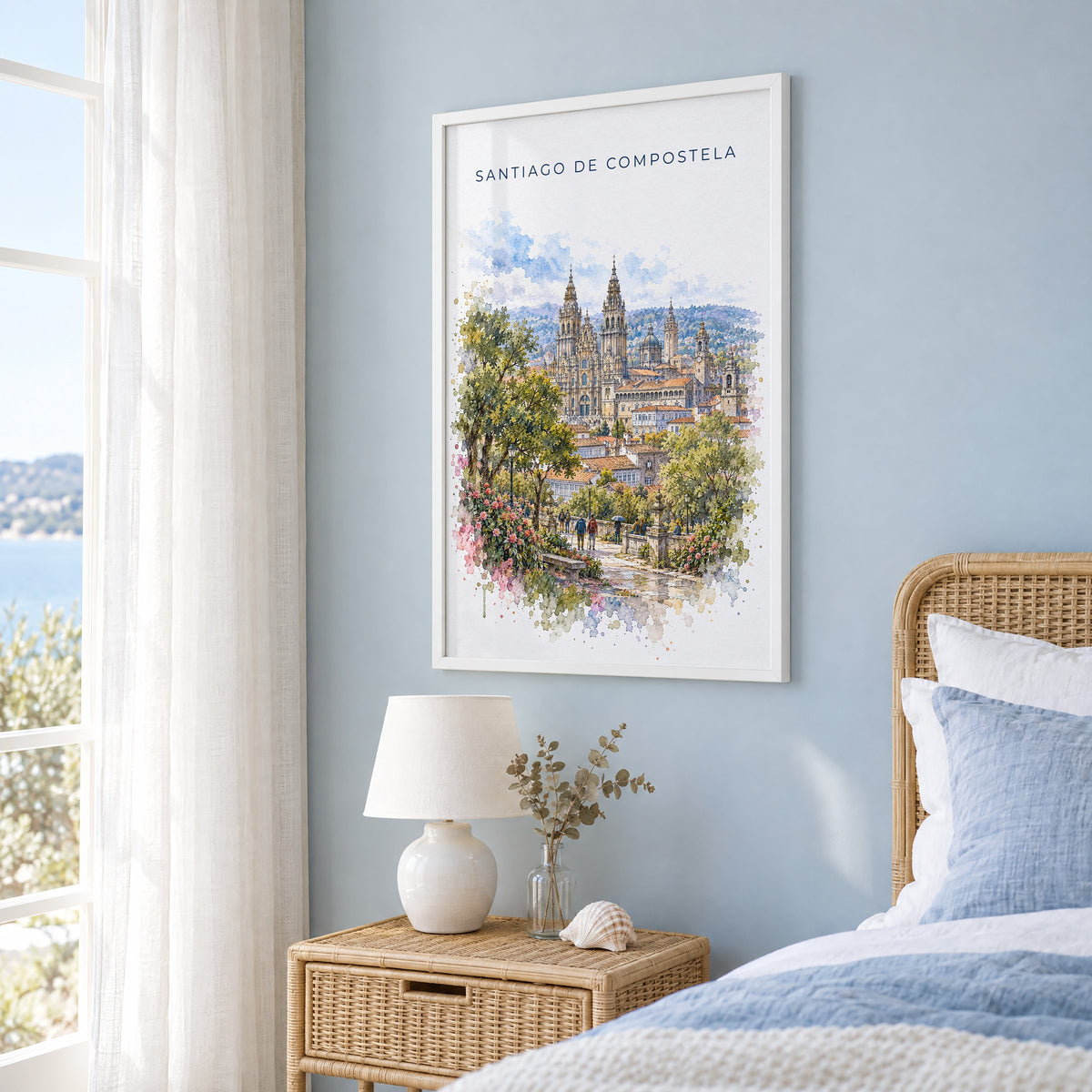 Santiago de Compostela watercolor print in a white frame on a pale blue wall beside a rattan bed in a coastal bedroom