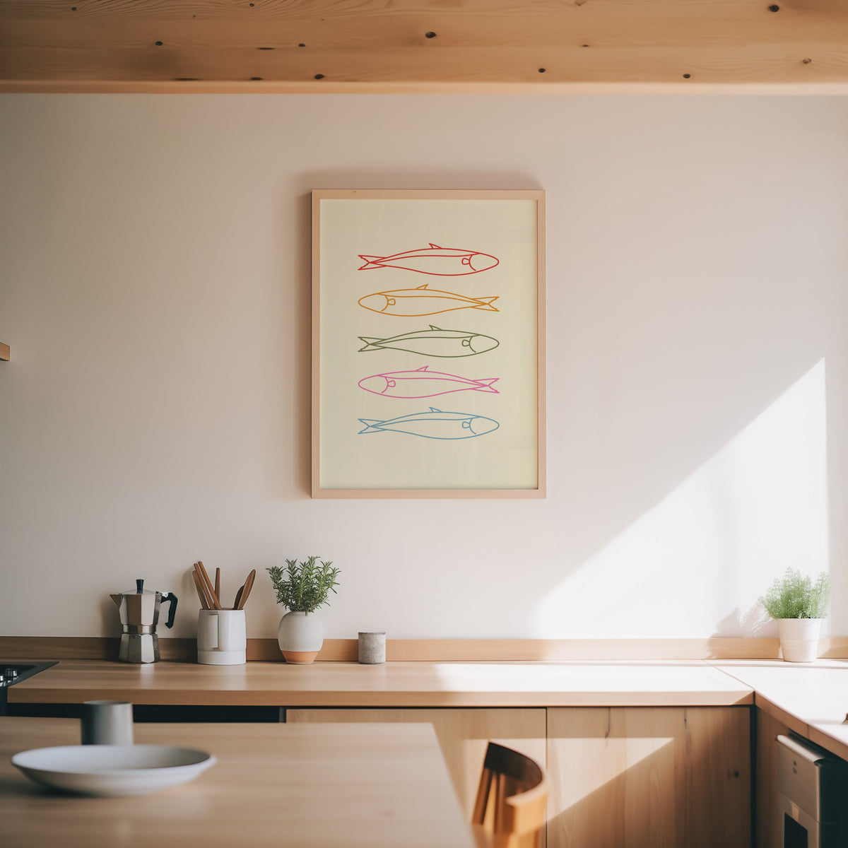Pastel sardine print in an oak frame above a wood counter with a moka pot and herbs