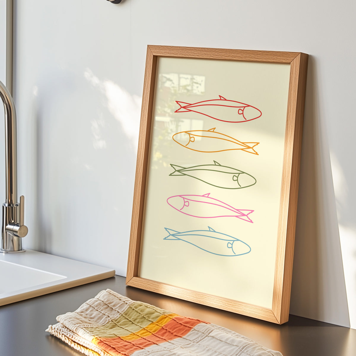 Pastel sardine print in an oak frame by the kitchen sink beside a striped tea towel