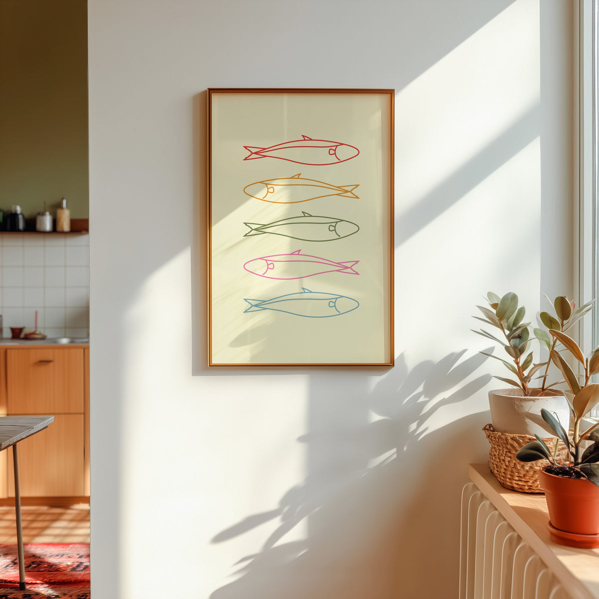 Pastel sardine print shown in a gold frame in sunlight with plants and a kitchen beyond