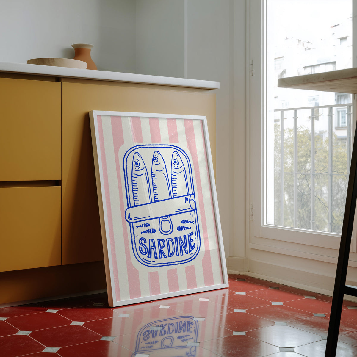 Sardine tin print in a white frame against yellow cabinets on a red tiled floor
