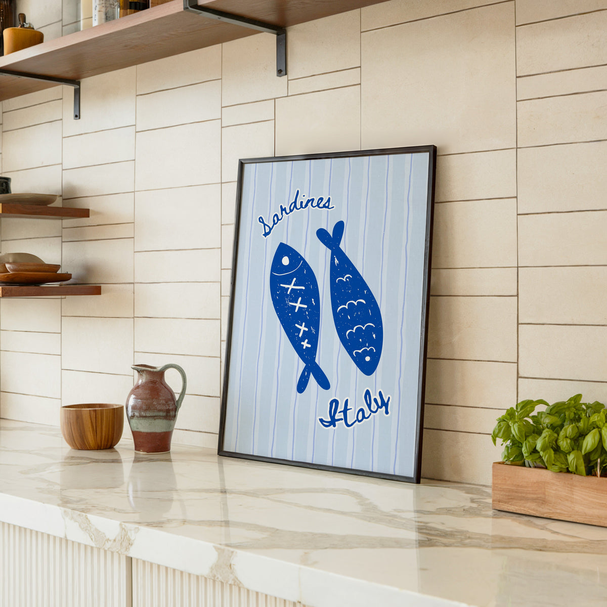 Sardines Italy print in a black frame leaning on a marble counter in a tiled kitchen