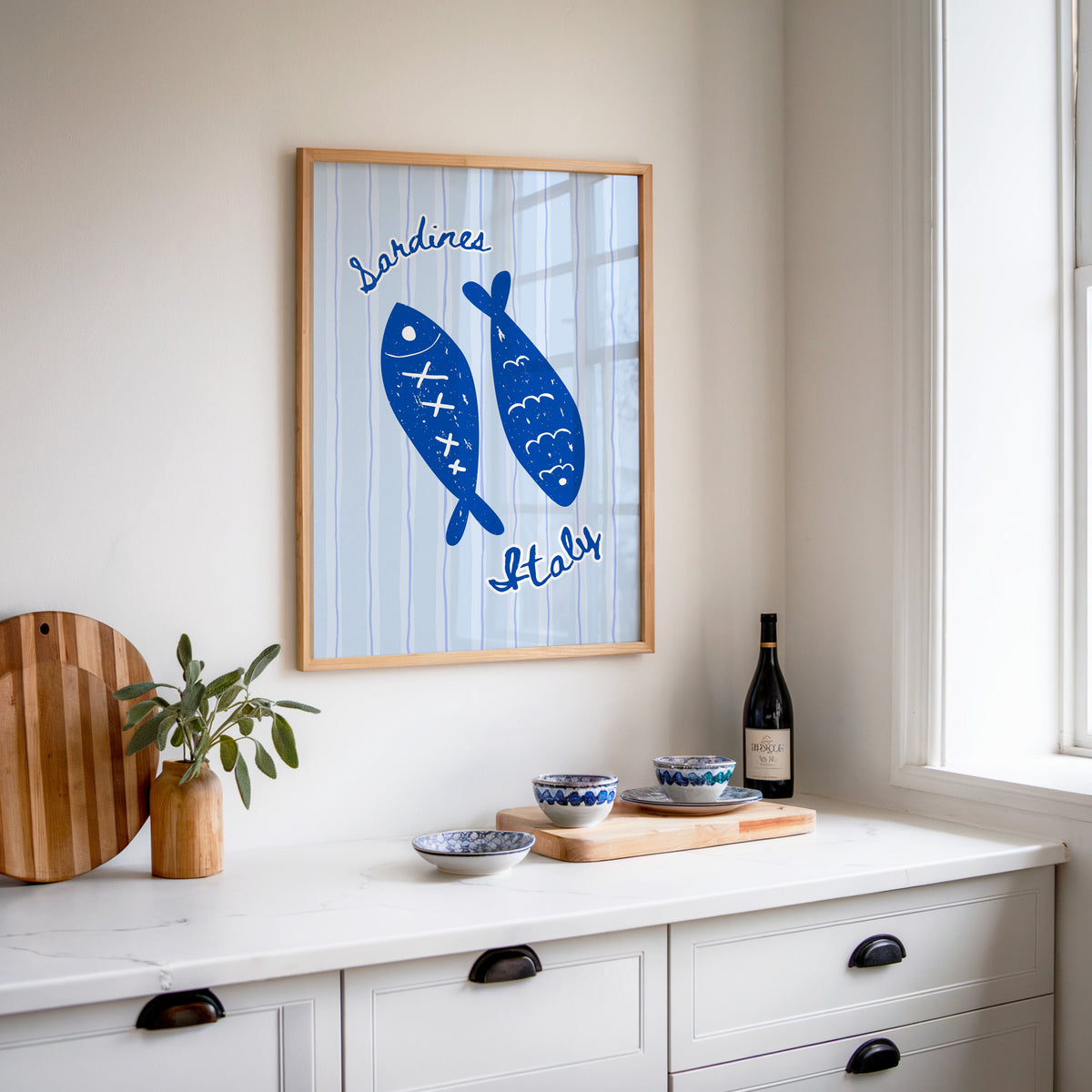 Sardines Italy print in an oak frame above a white sideboard with a bottle of wine