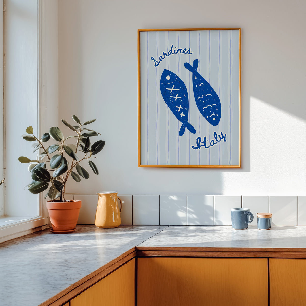 Sardines Italy print shown in a gold frame above a marble counter in a tan kitchen