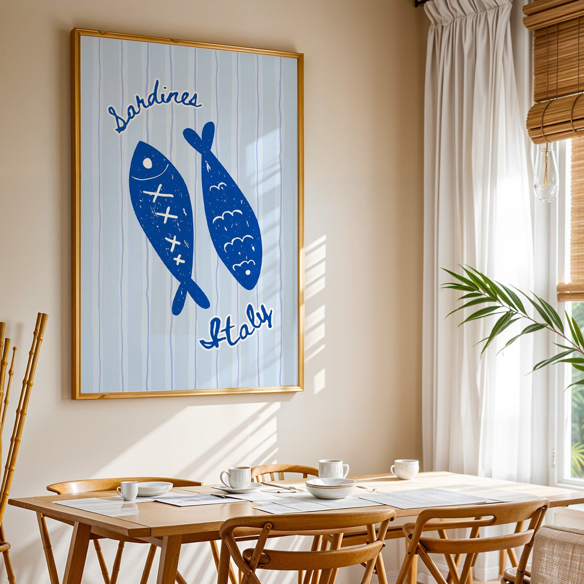 Sardines Italy print shown in a gold frame above a breakfast table by a curtained window