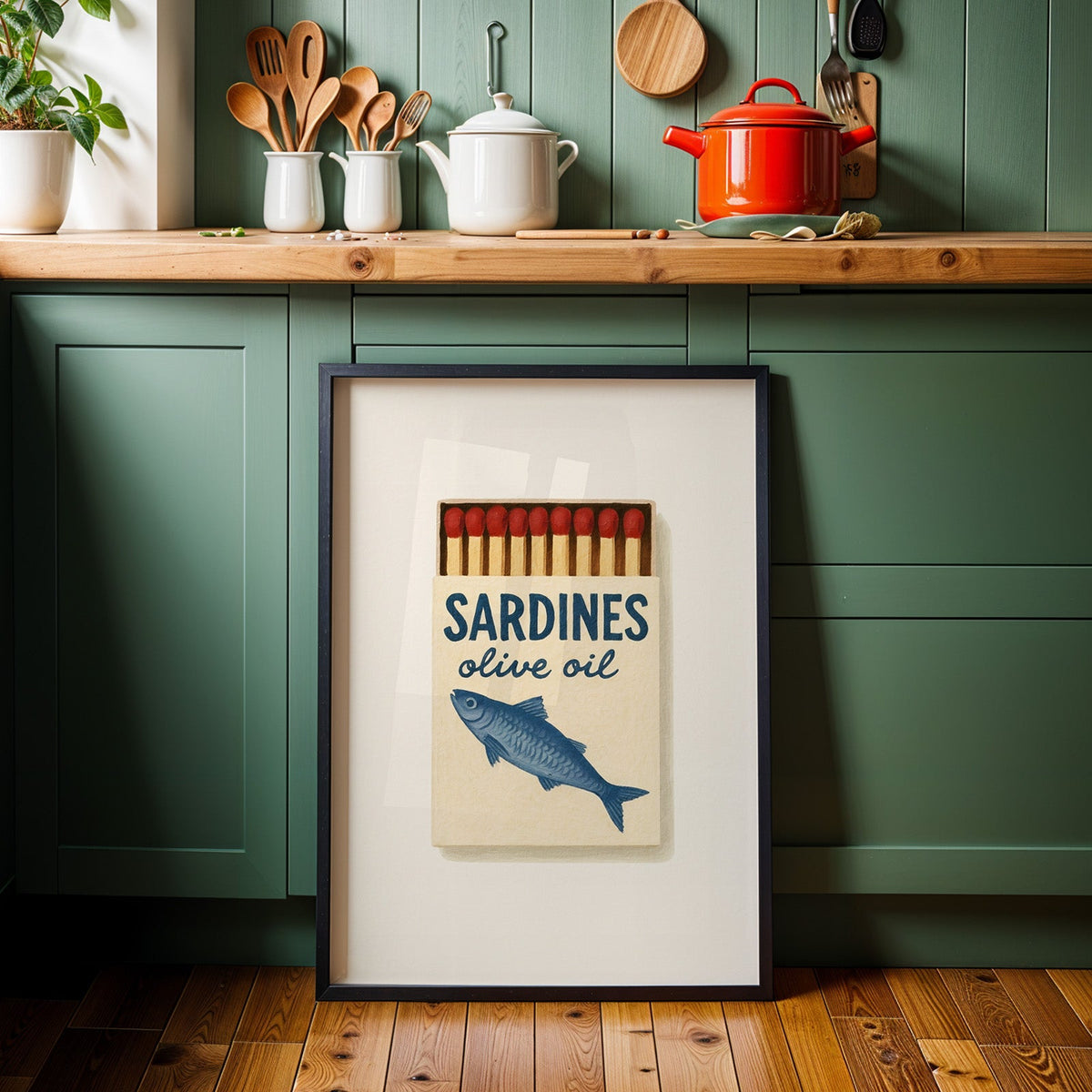 Sardines olive oil matchbox print in a black frame against sage green kitchen cabinets