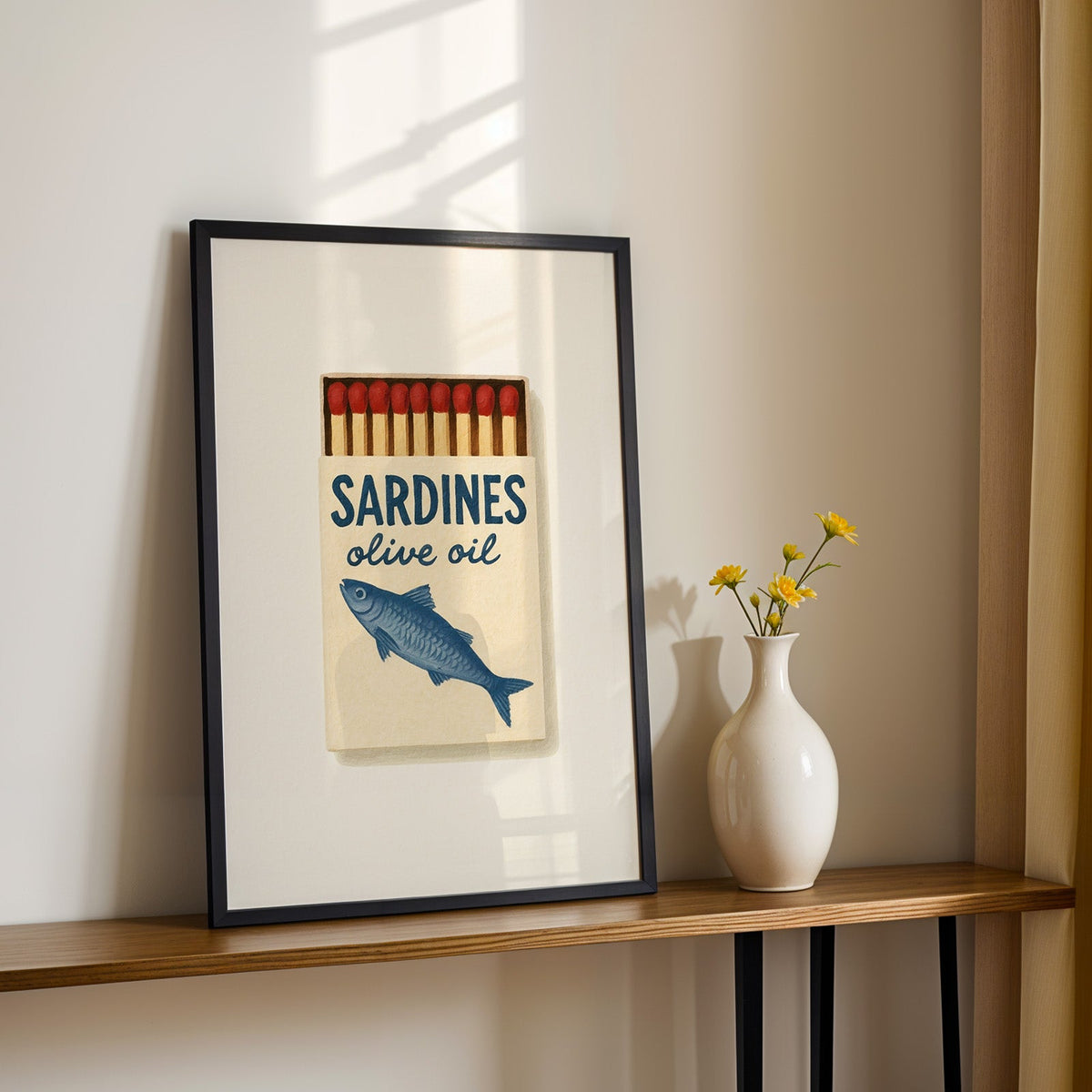Sardines olive oil matchbox print in a black frame on a console table with daisies
