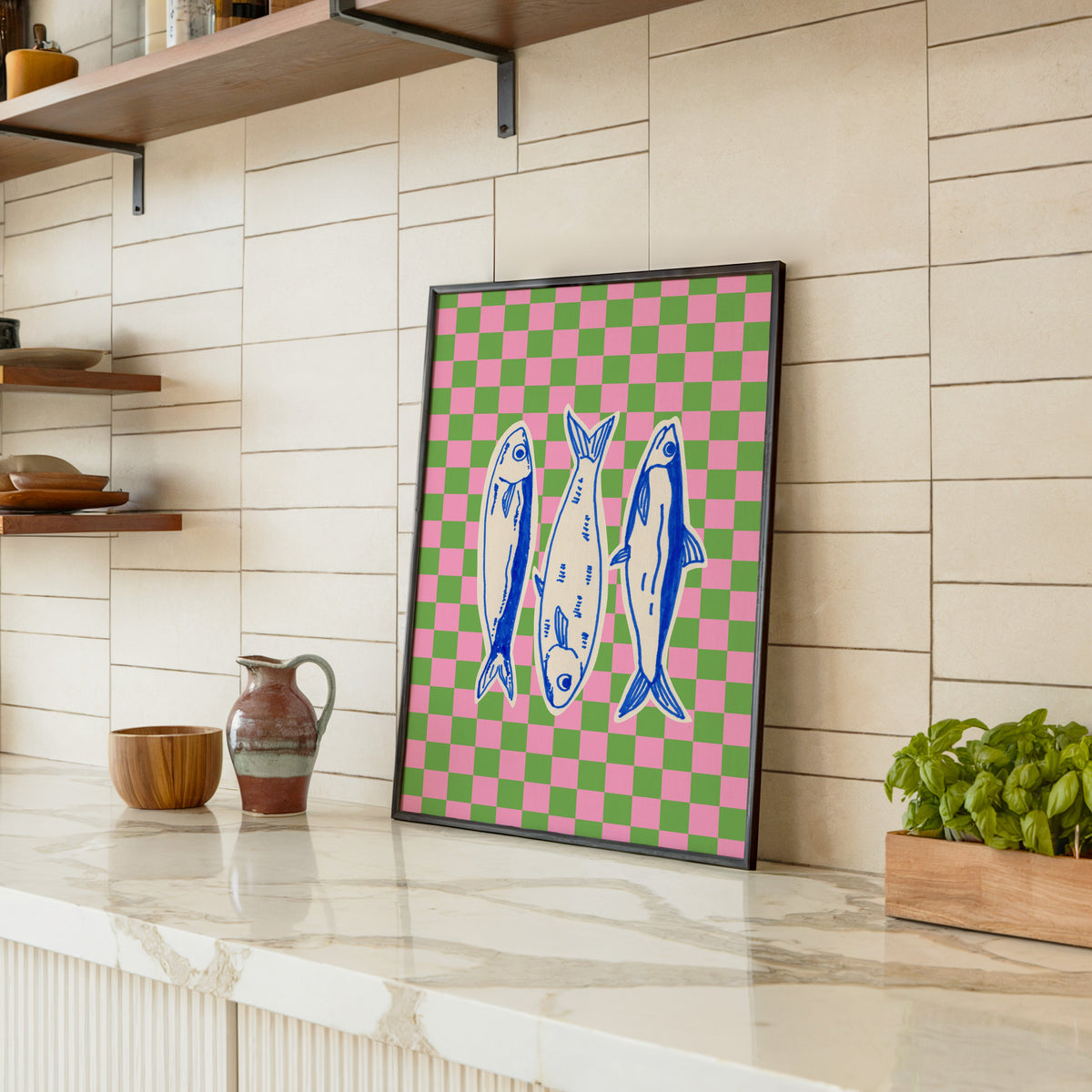 Sardines checkerboard print in a black frame leaning on a marble counter in a tiled kitchen
