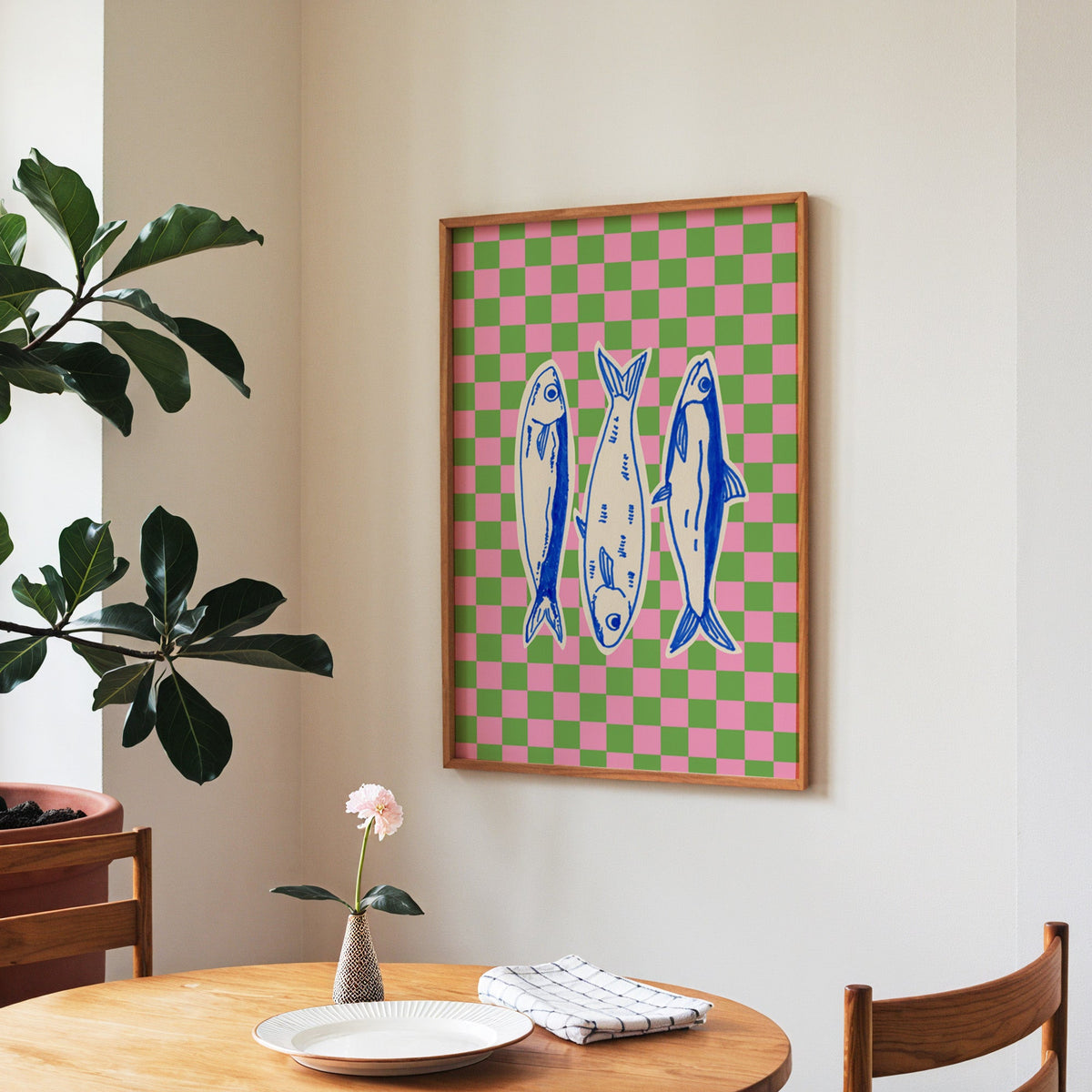 Sardines checkerboard print in a walnut frame above a round table beside a fiddle-leaf fig