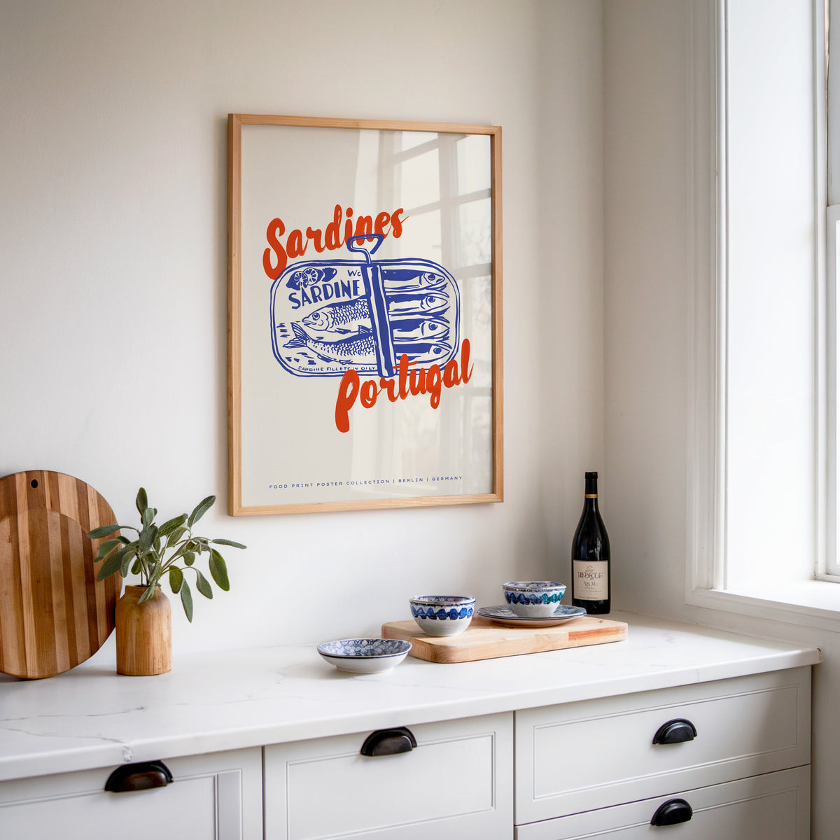 Blue sardine tin print in an oak frame above a white kitchen sideboard