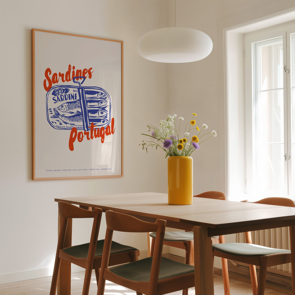 Blue sardine tin print in a slim oak frame above a dining table