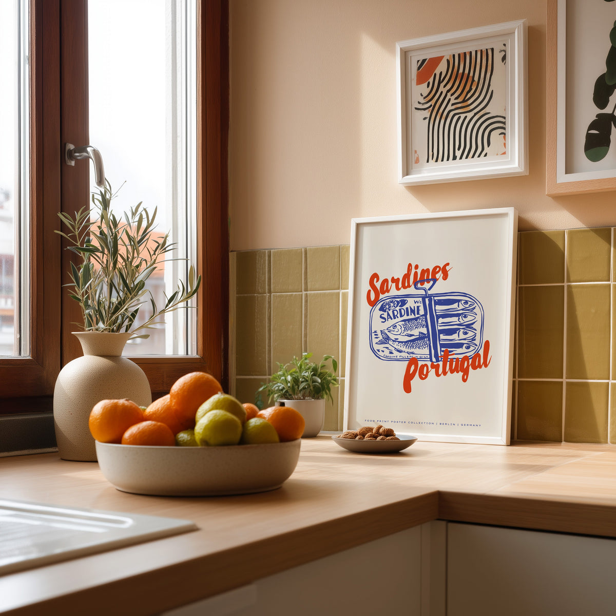Blue sardine tin print in a white frame against olive green kitchen tiles