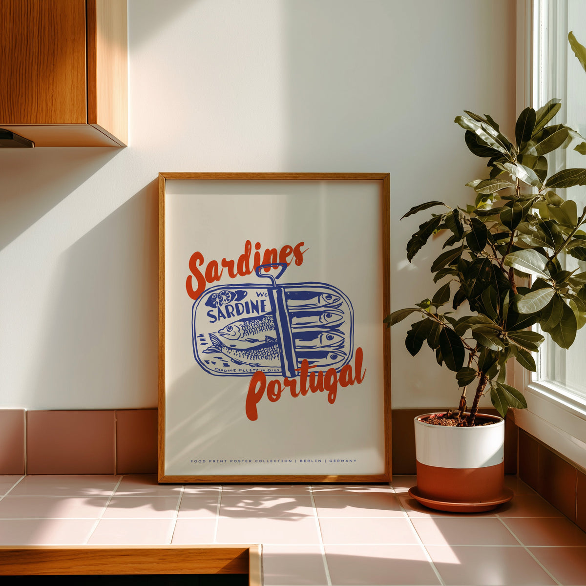 Blue sardine tin print in an oak frame on pink tiles in afternoon sun