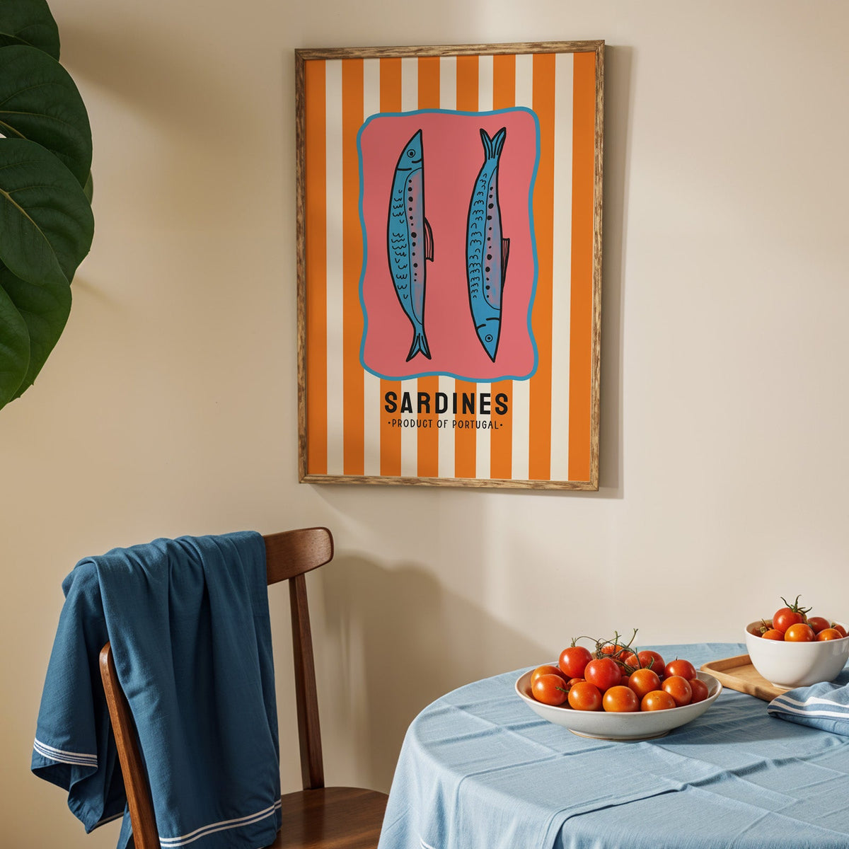 Sardines of Portugal print in an oak frame above a blue linen table with ripe tomatoes