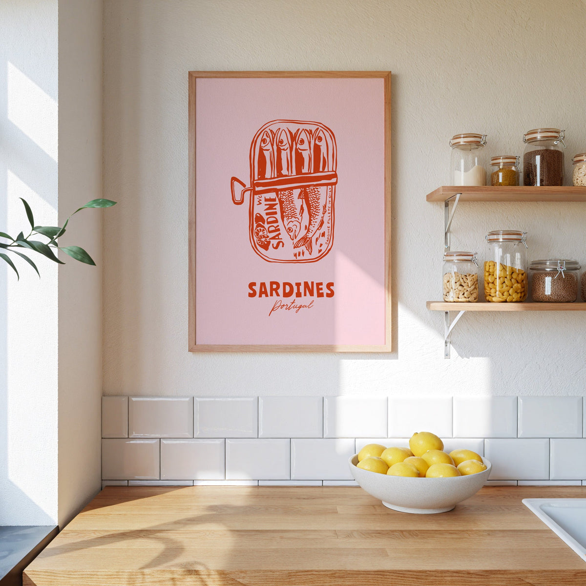 Pink sardine tin print in an oak frame on a kitchen wall beside open shelves