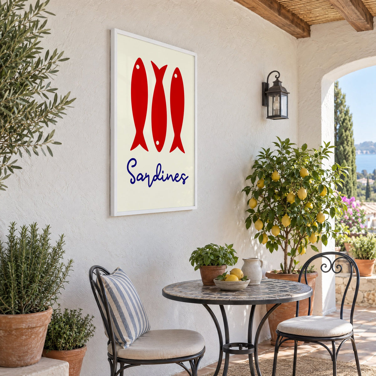 Three red sardines print in a white frame on a sunny patio wall beside a potted lemon tree