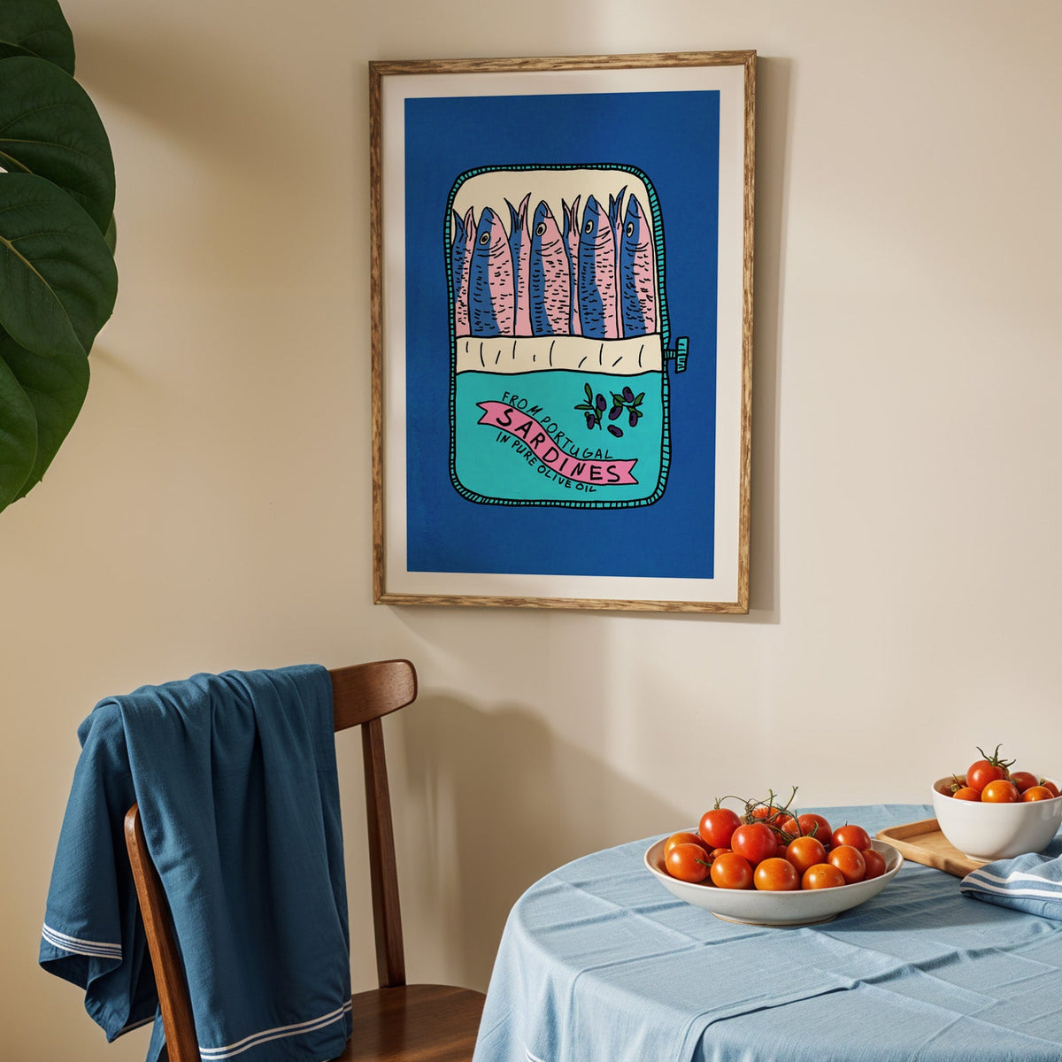 Blue sardine tin print in an oak frame above a blue linen table with ripe tomatoes