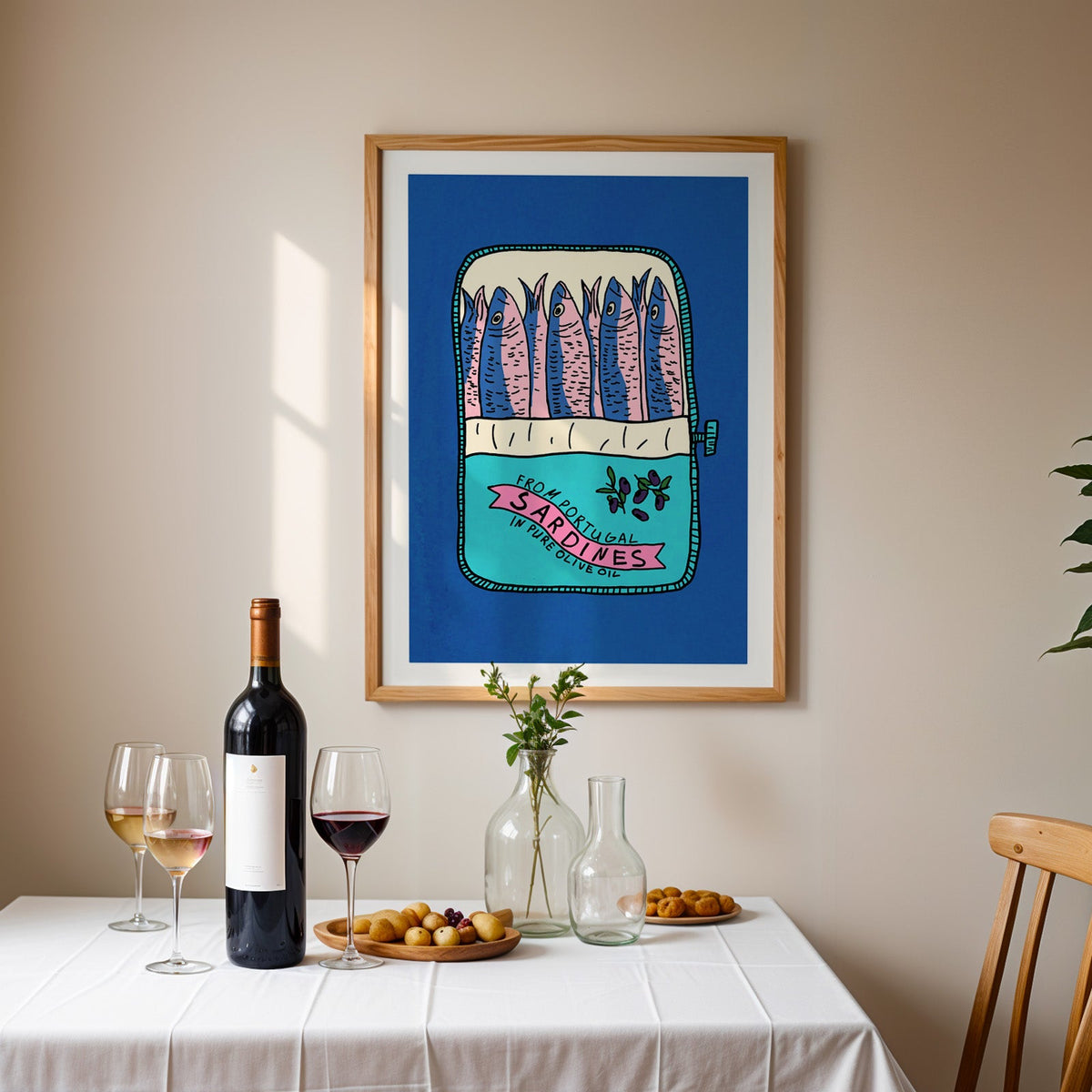 Blue sardine tin print in an oak frame above a table laid with red wine and glasses