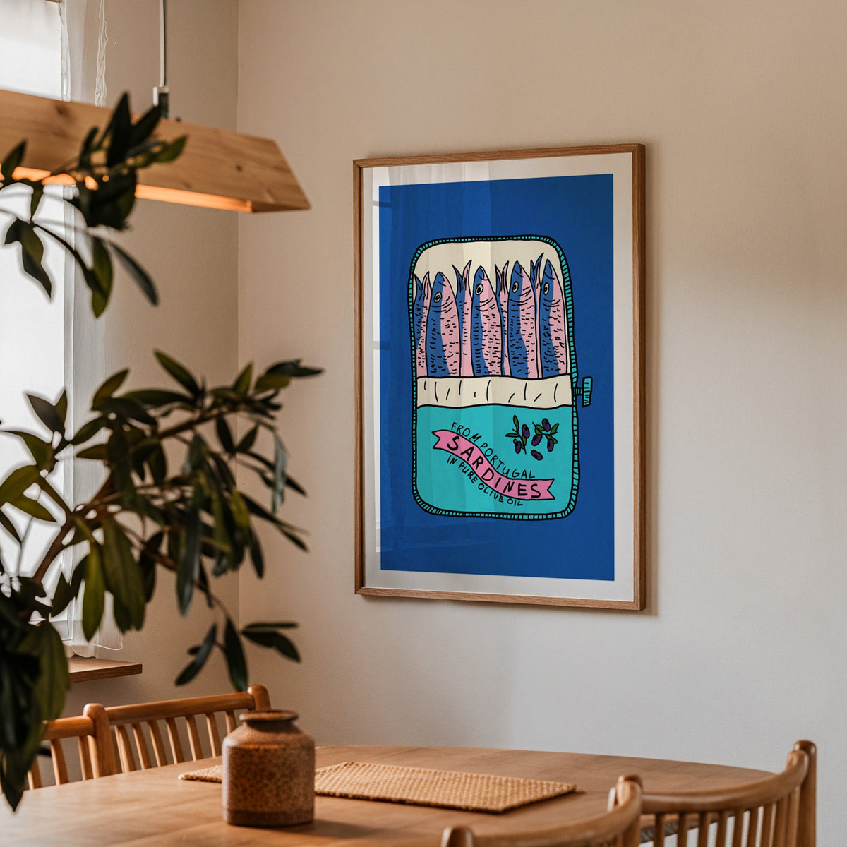 Blue sardine tin print in a walnut frame above a dining table beside an olive tree