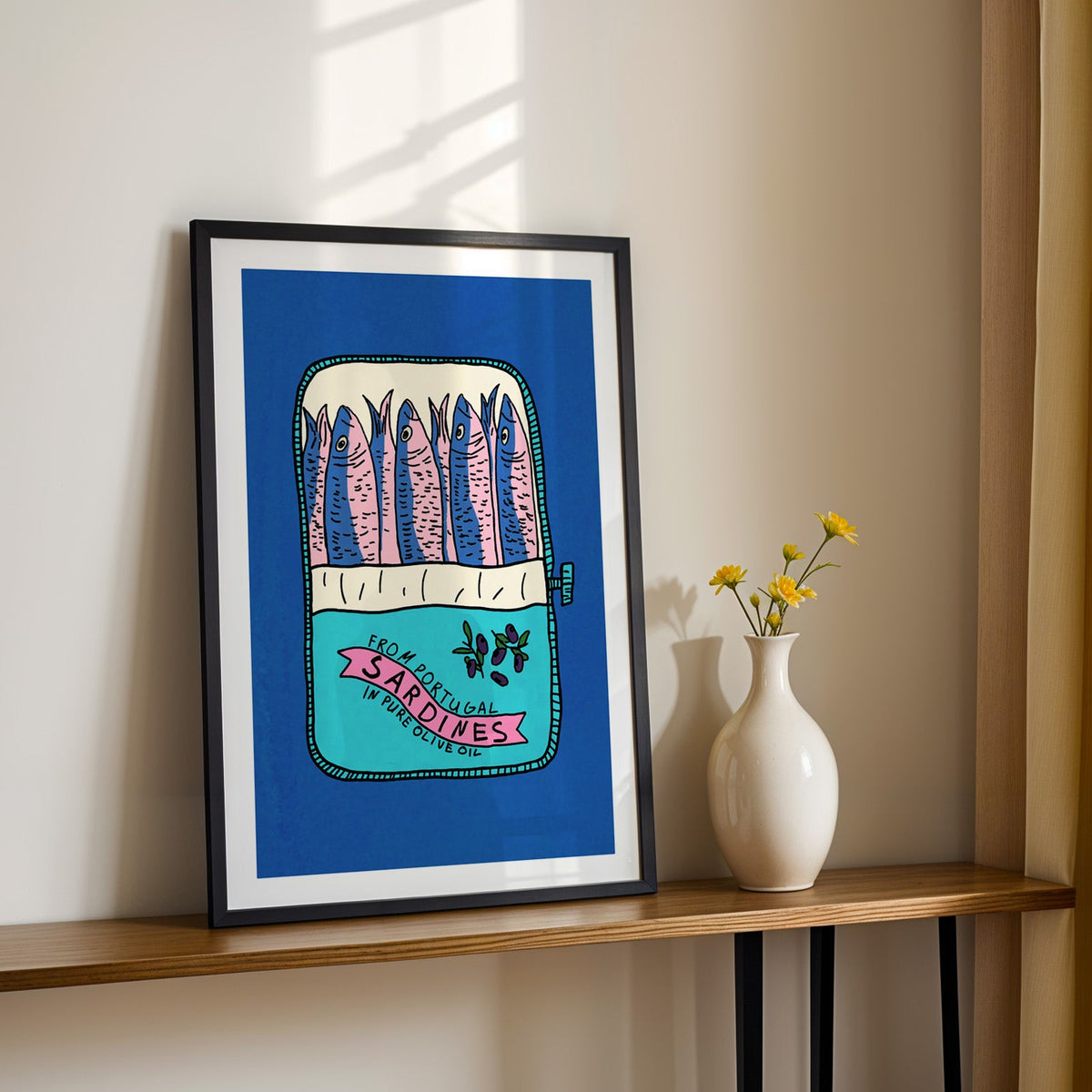 Blue sardine tin print in a black frame on a console table with yellow daisies