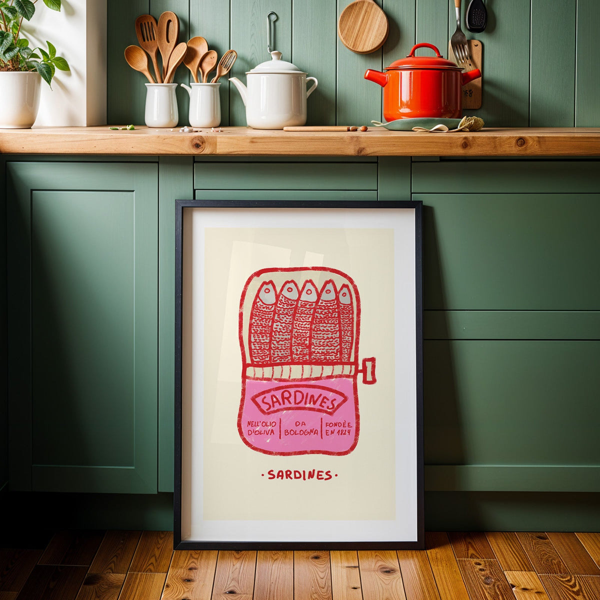 Pink sardine tin print in a black frame against sage green kitchen cabinets