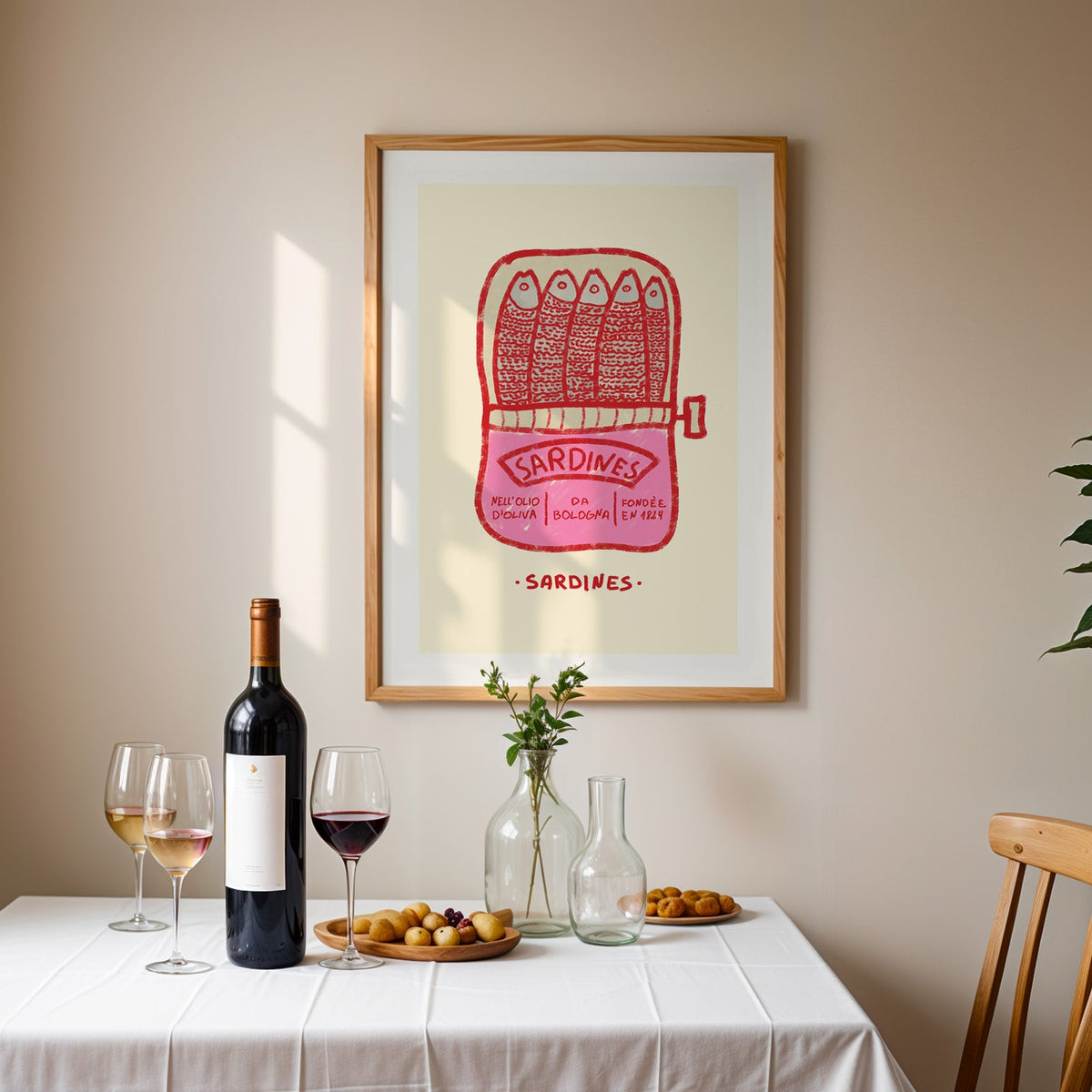 Pink sardine tin print in an oak frame above a table laid with red wine and glasses