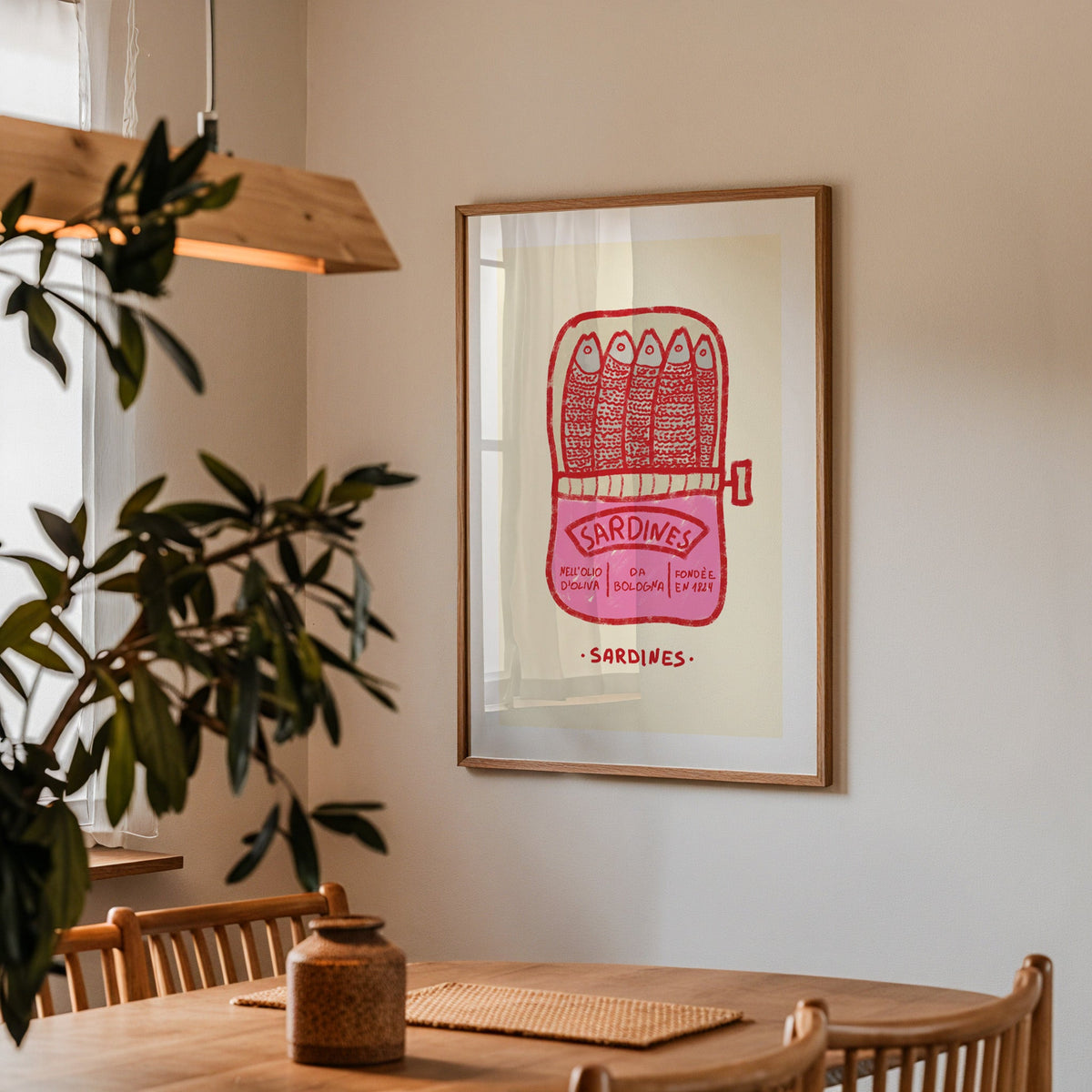 Pink sardine tin print in a walnut frame above a dining table beside an olive tree