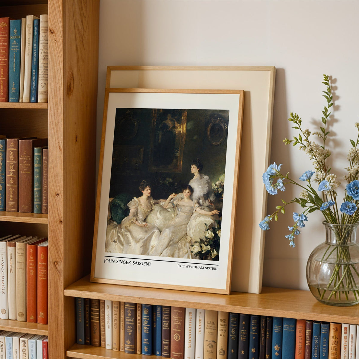 Three sisters in white gowns print in an oak frame leaning on a bookshelf beside flowers